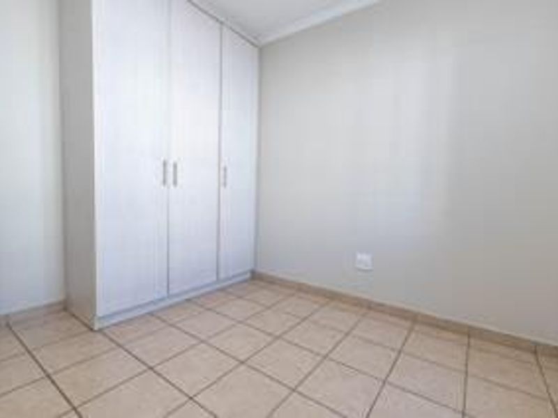 A clean, empty bedroom featuring neutral tiled flooring and a functional built-in wardrobe, offering a blank canvas for personalization.