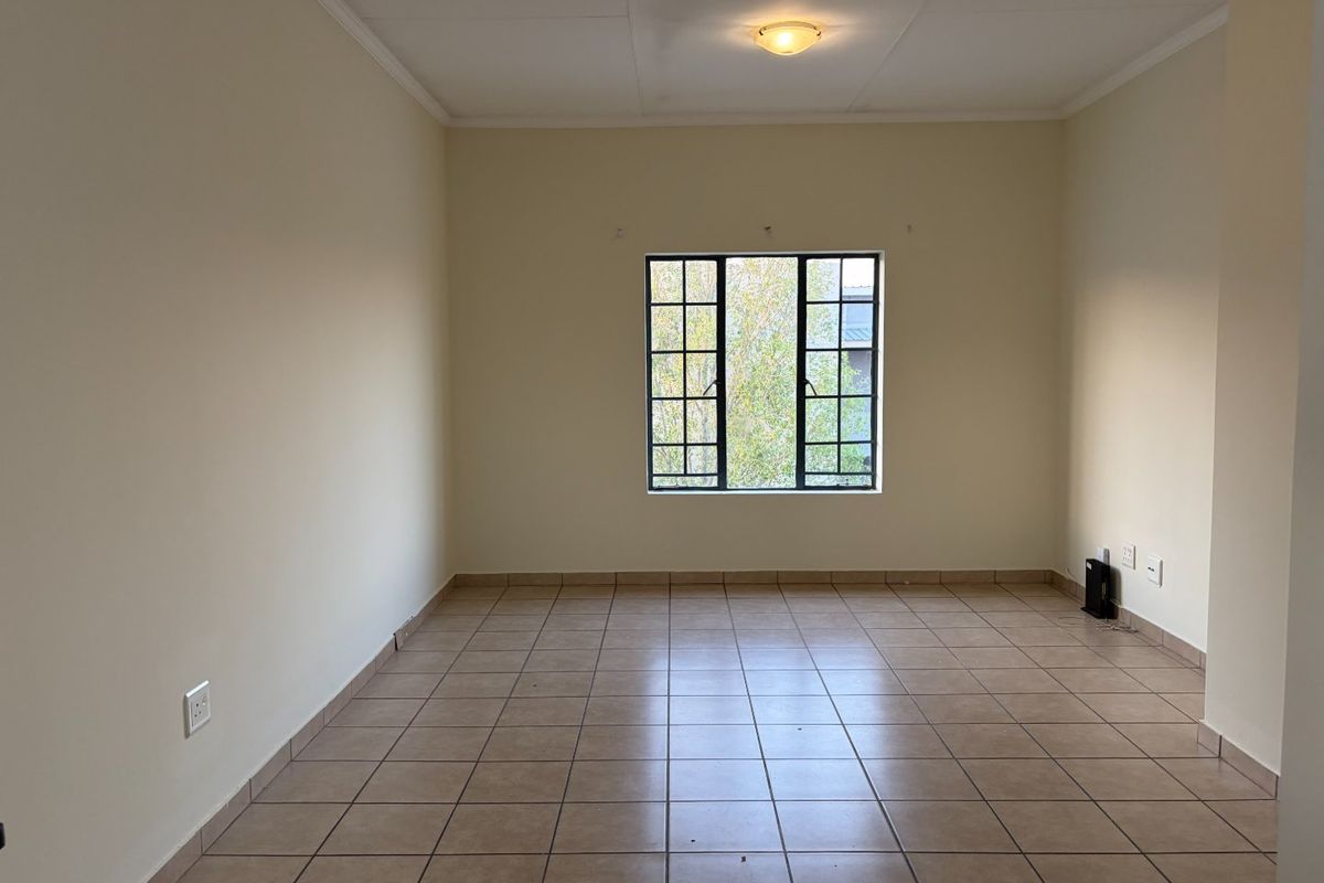 A bright, empty living room featuring neutral walls, tiled flooring, and a large grid-pattern window providing natural light.
