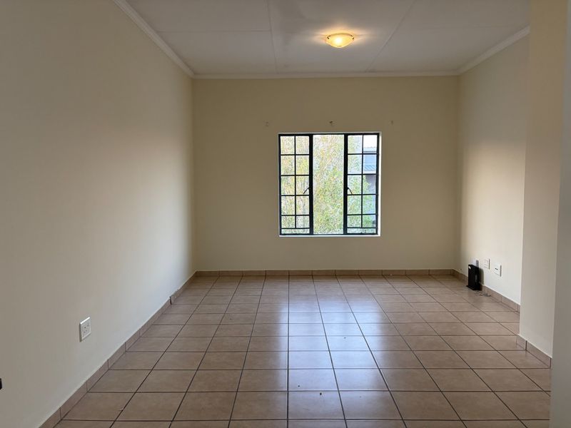 A bright, empty living room featuring neutral walls, tiled flooring, and a large grid-pattern window providing natural light.