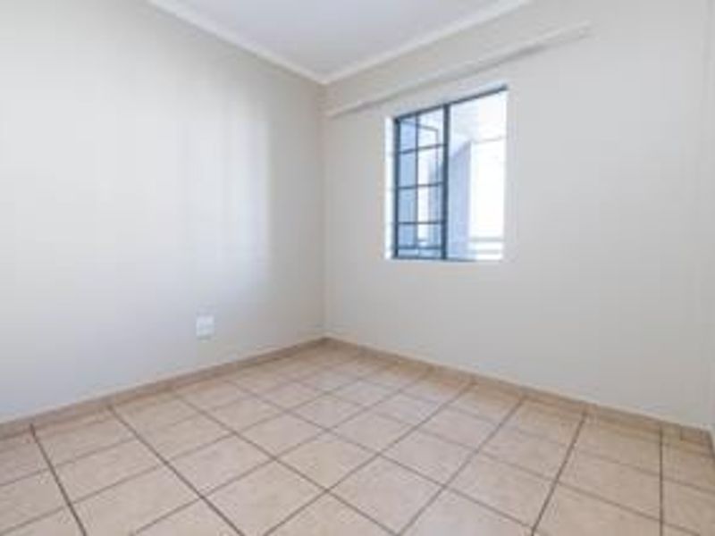 A bright, empty bedroom featuring neutral walls, tiled flooring, and a window fitted with security bars.