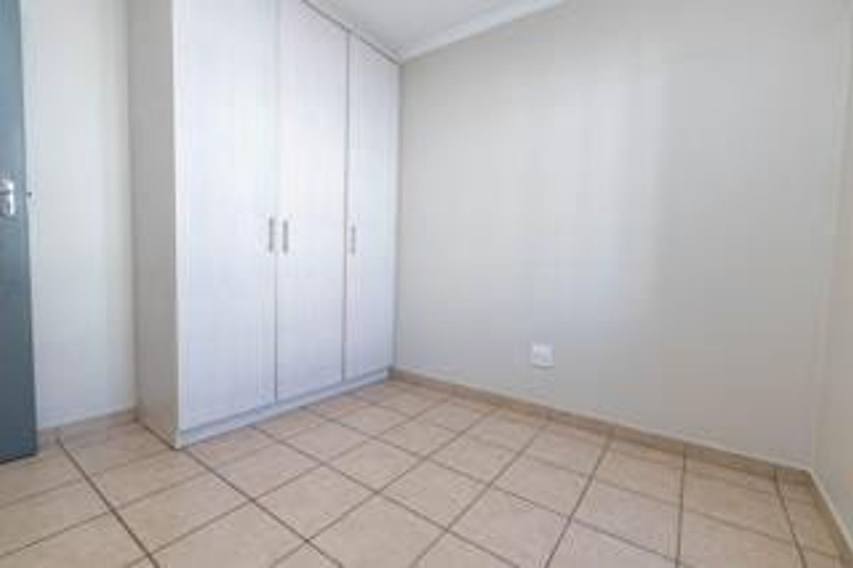 A clean, empty bedroom featuring neutral tiled flooring and a functional built-in wardrobe, offering a blank canvas for personalization.