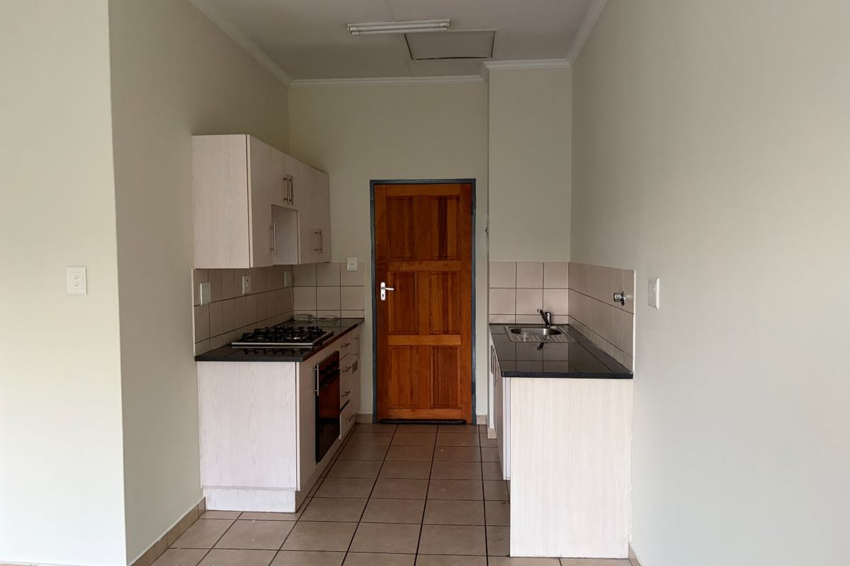 A functional kitchen featuring light-toned cabinetry, granite countertops, a gas hob, built-in oven, and tiled flooring, presented in a clean, vacant state.