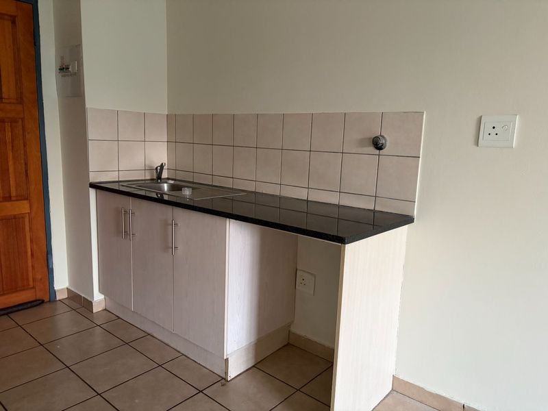 A compact kitchen area featuring built-in cabinetry, a granite countertop with an integrated stainless steel sink, and neutral tiled backsplash.