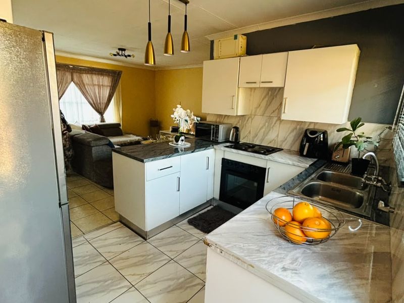 Open-plan kitchen and living area featuring white cabinetry, marble-effect countertops, tiled flooring, and modern pendant lighting in a functional townhouse layout.