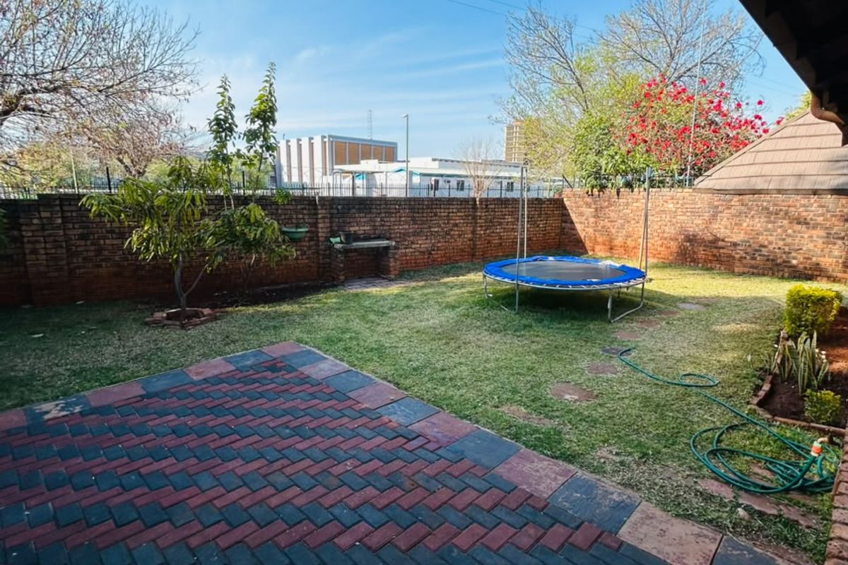 A private rear garden featuring a paved patio area, lawn, and a built-in brick braai, enclosed by a perimeter wall.