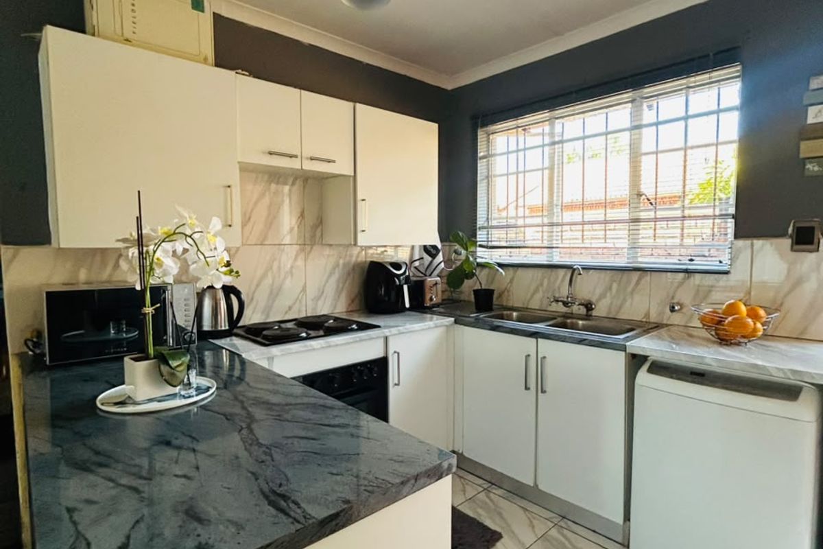 A well-maintained kitchen featuring white cabinetry, dark stone countertops, tiled flooring, and a double basin sink with security bars on the window.
