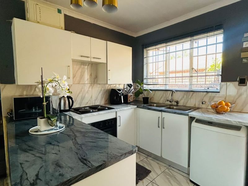 A well-maintained kitchen featuring white cabinetry, dark stone countertops, tiled flooring, and a double basin sink with security bars on the window.