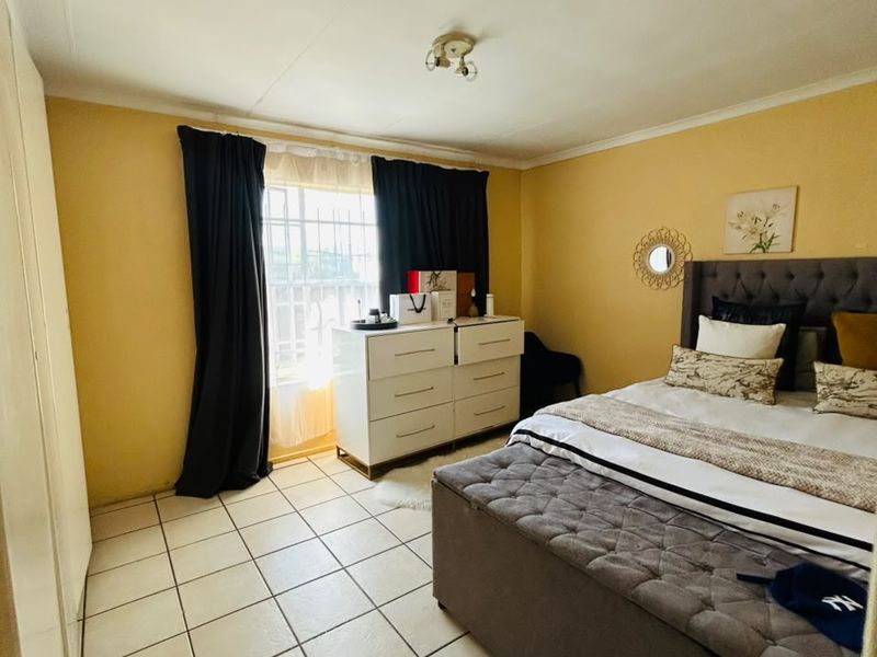 A bedroom featuring tiled flooring, built-in cupboards, and a window fitted with security bars.