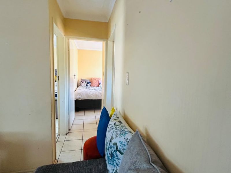 A narrow hallway with tiled flooring leading towards a bedroom, featuring plain walls and coving.