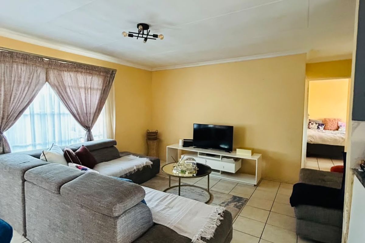 A living room featuring tiled flooring and neutral wall finishes, providing a functional and comfortable space with direct access to an adjacent bedroom.