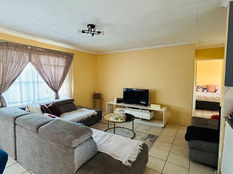 A living room featuring tiled flooring and neutral wall finishes, providing a functional and comfortable space with direct access to an adjacent bedroom.