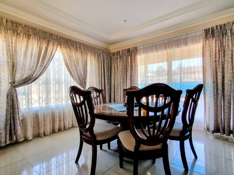 A bright dining room featuring polished tiled flooring, coved ceiling details, and large windows that provide ample natural light.
