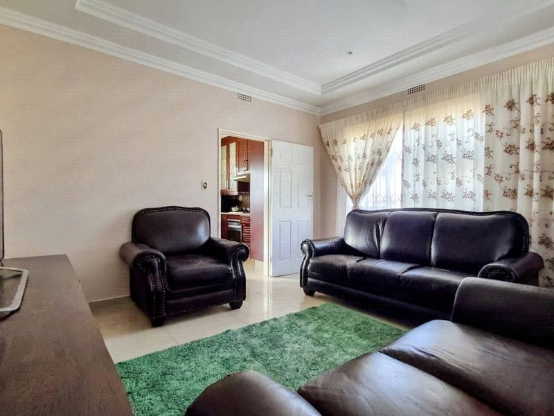 A comfortable living room featuring tiled flooring, crown molding, and direct access to the kitchen area.