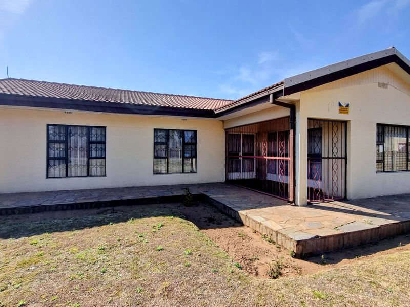 Front elevation of a single-story house featuring a tiled roof, stone patio area, and security gates over windows and entrance.
