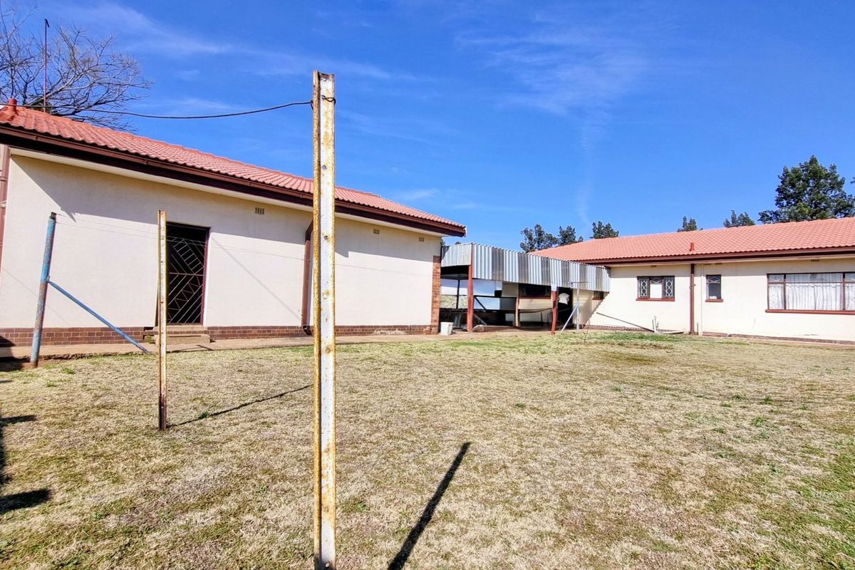 Rear view of the property showing the backyard, tiled roof structures, a metal carport, and exterior wall finishes.