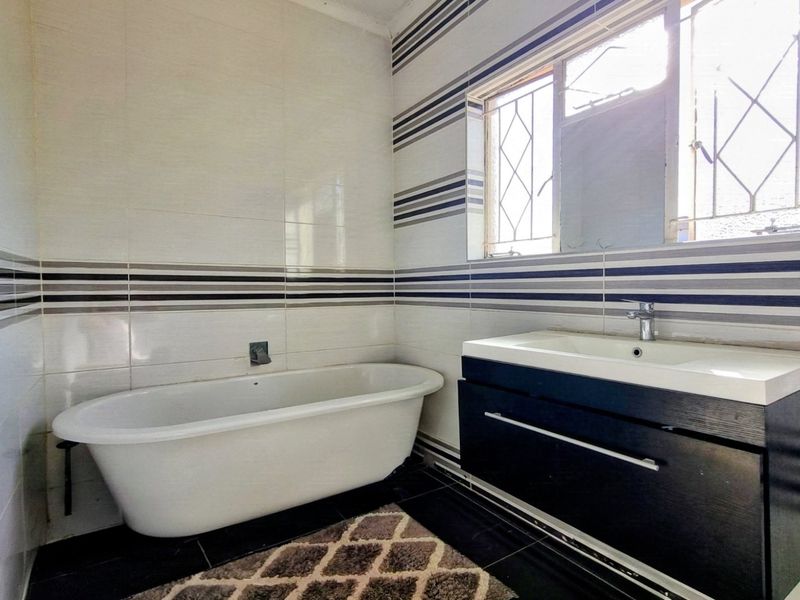 A clean bathroom featuring a freestanding bathtub, a modern wall-mounted vanity with basin, and decorative horizontal-striped wall tiling.