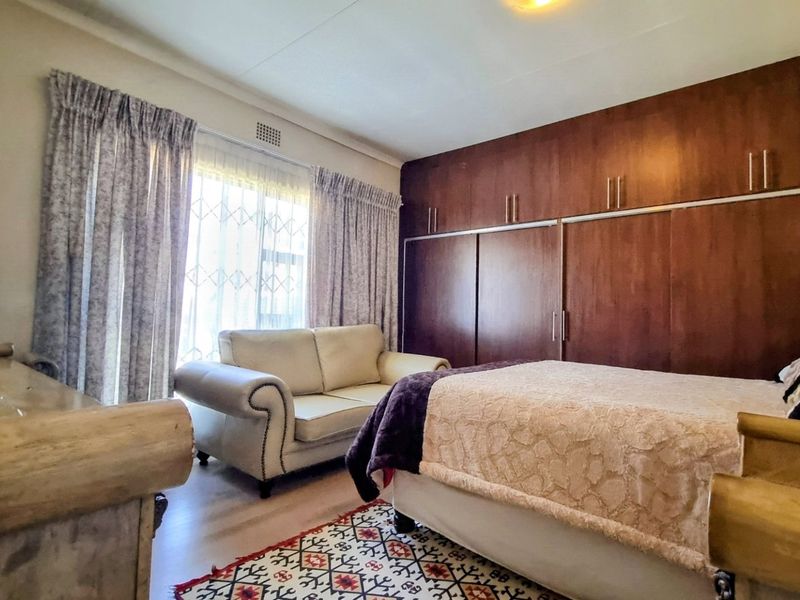 A spacious bedroom featuring extensive built-in wooden cupboards, laminate flooring, and large windows with curtain rails.