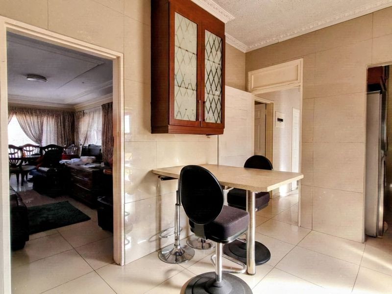 A kitchen area featuring tiled walls and flooring, with wall-mounted cabinetry and crown molding, providing access to adjacent living spaces.
