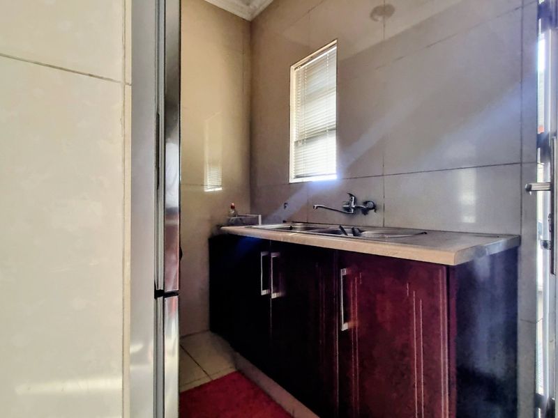 A functional scullery area featuring dark wood-finish cabinetry, a stainless steel sink, and tiled wall finishes with natural light.