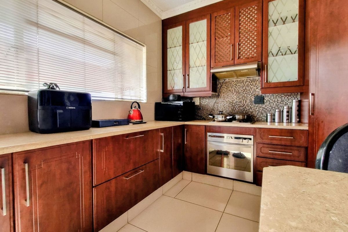 A functional kitchen featuring dark wood cabinetry, stone countertops, a mosaic tile backsplash, and integrated appliances including an oven and hob.