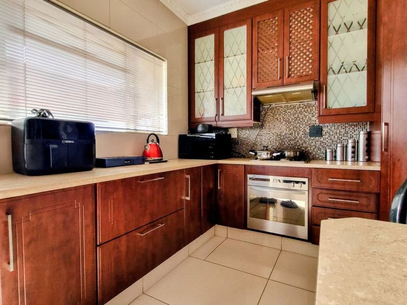 A functional kitchen featuring dark wood cabinetry, stone countertops, a mosaic tile backsplash, and integrated appliances including an oven and hob.