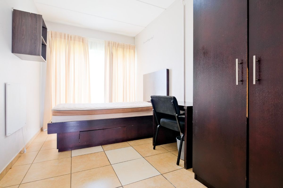 A functional bedroom featuring tiled flooring, a built-in wardrobe, and wall-mounted storage, offering a practical layout for a commercial or residential space.