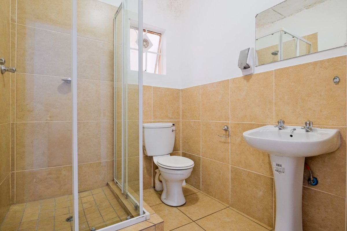 A functional bathroom featuring a shower enclosure, pedestal sink, and toilet with neutral wall and floor tiling.