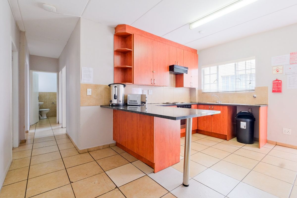 A functional commercial kitchen featuring laminate cabinetry, granite countertops, and ceramic tiled flooring, with an adjacent hallway leading to a restroom.