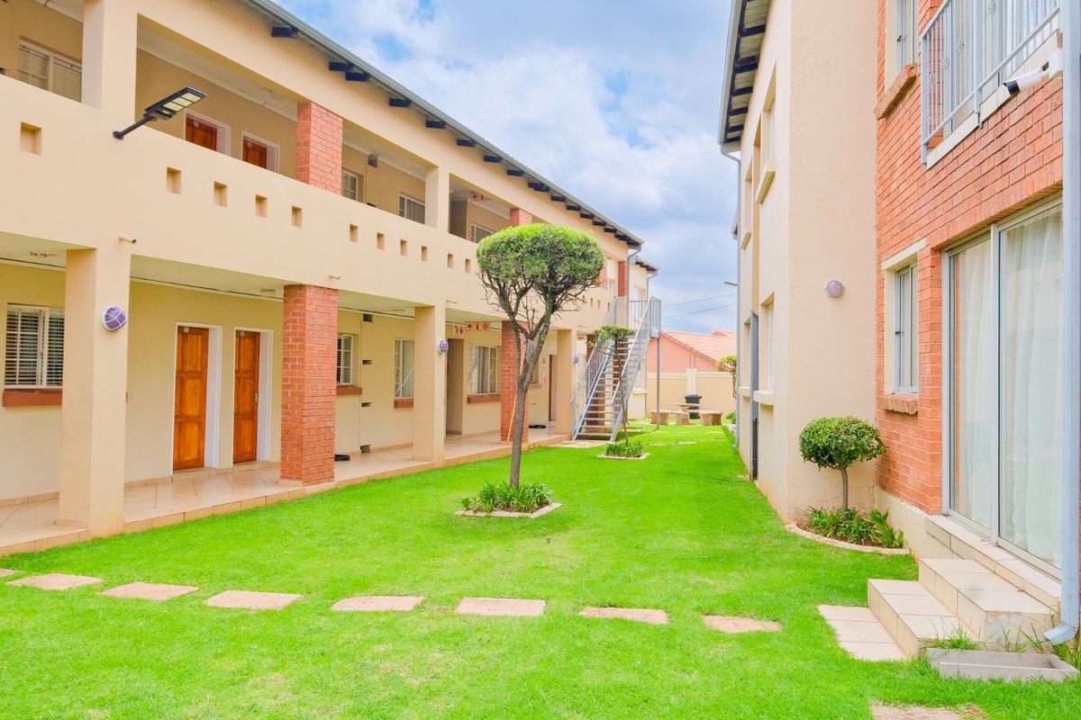 A well-maintained exterior courtyard area featuring a central lawn, brick-pillared walkways, and metal stair access between commercial building units.