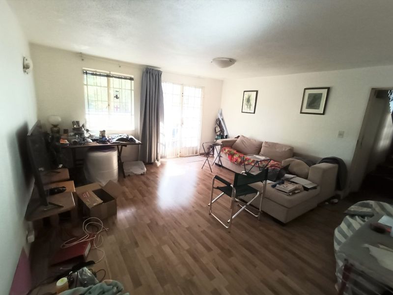 A living room featuring laminate flooring, a sliding glass door with security gate, and a window with security bars.