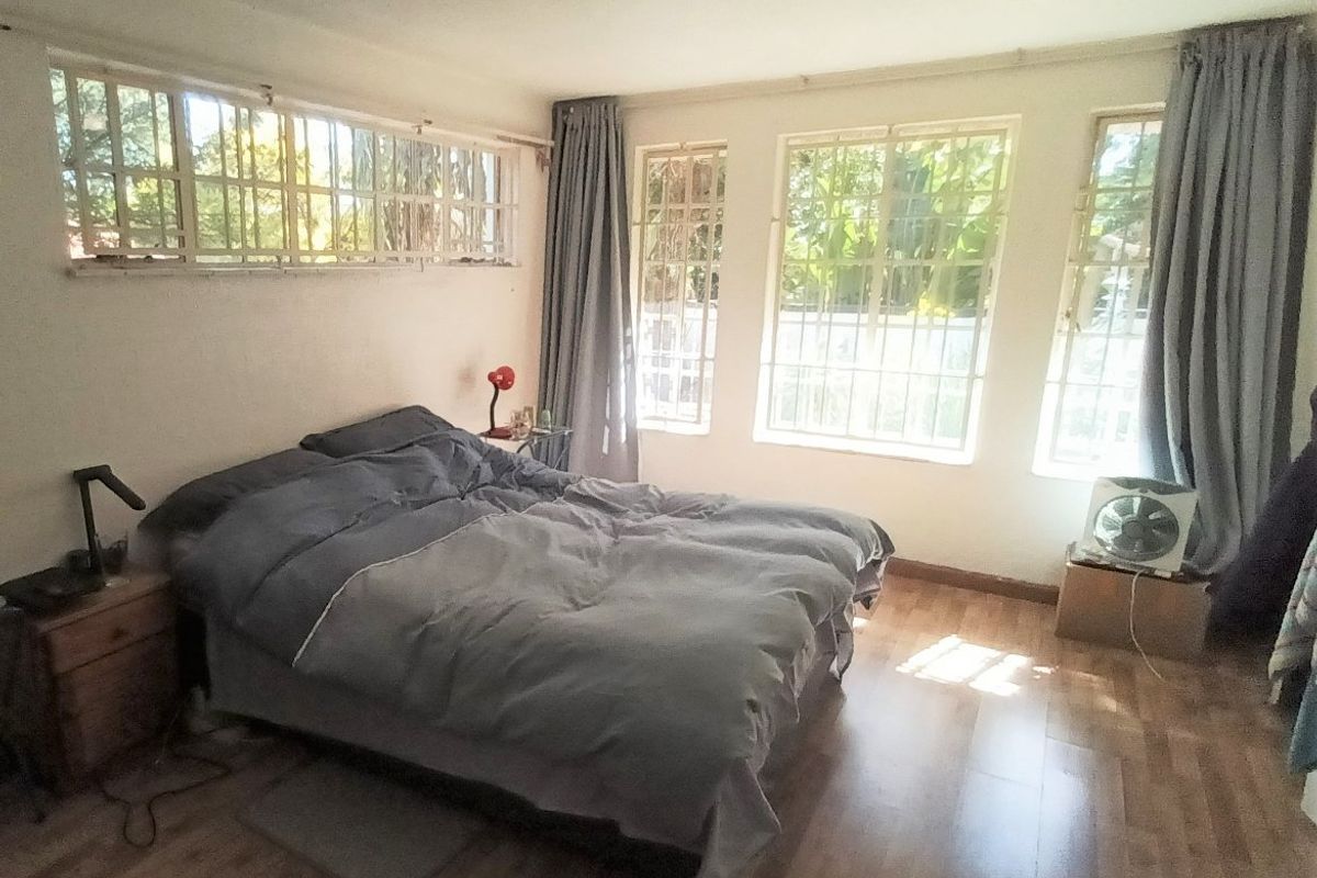 A bedroom featuring laminate flooring, multiple windows with security bars, and a ceiling light fixture.