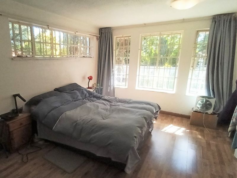 A bedroom featuring laminate flooring, multiple windows with security bars, and a ceiling light fixture.