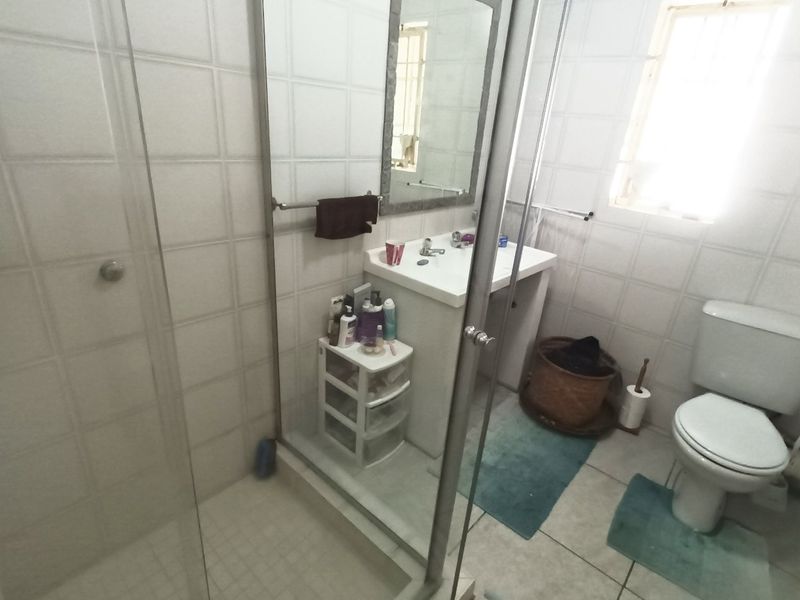A functional bathroom featuring a glass shower enclosure, pedestal basin, and toilet with neutral wall and floor tiling.