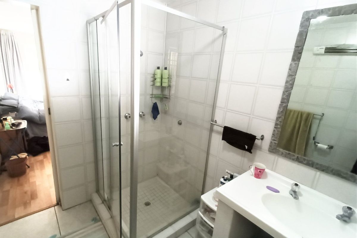A functional bathroom featuring a glass-enclosed shower, a vanity basin with a wall-mounted mirror, and neutral wall tiling.