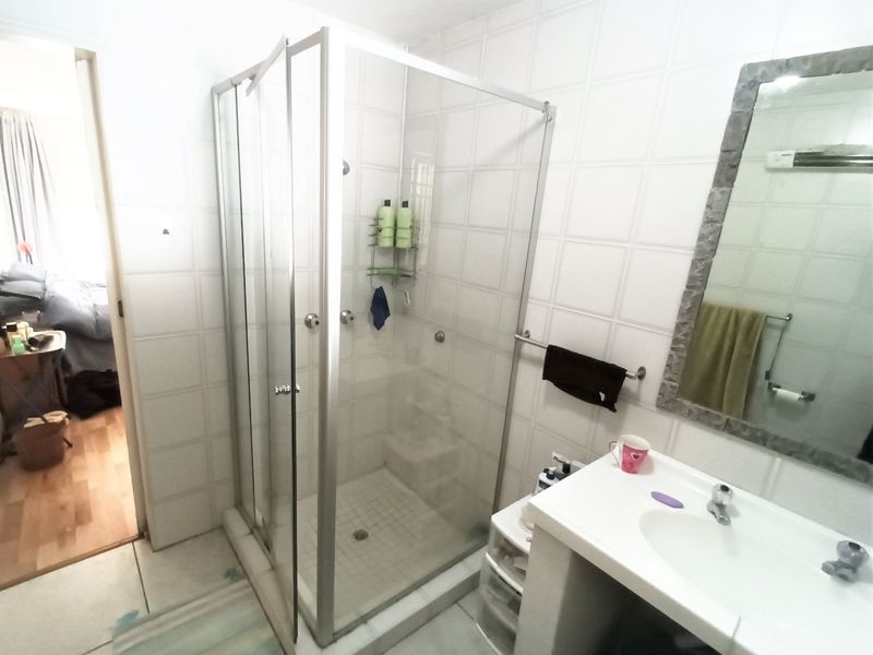 A functional bathroom featuring a glass-enclosed shower, a vanity basin with a wall-mounted mirror, and neutral wall tiling.