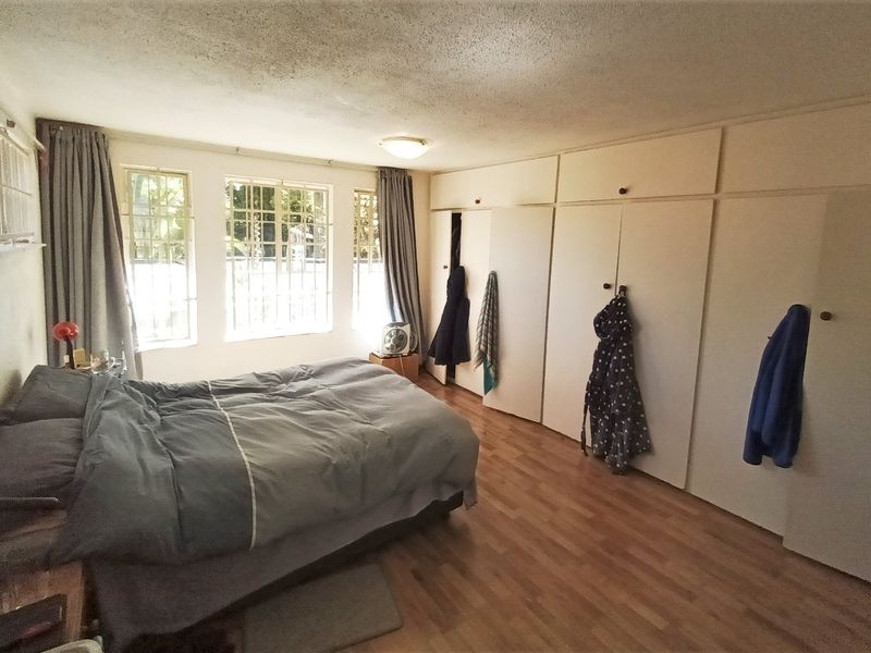 A spacious bedroom featuring extensive built-in cupboards, laminate flooring, and large windows with security bars, offering a functional layout with potential for modernization.