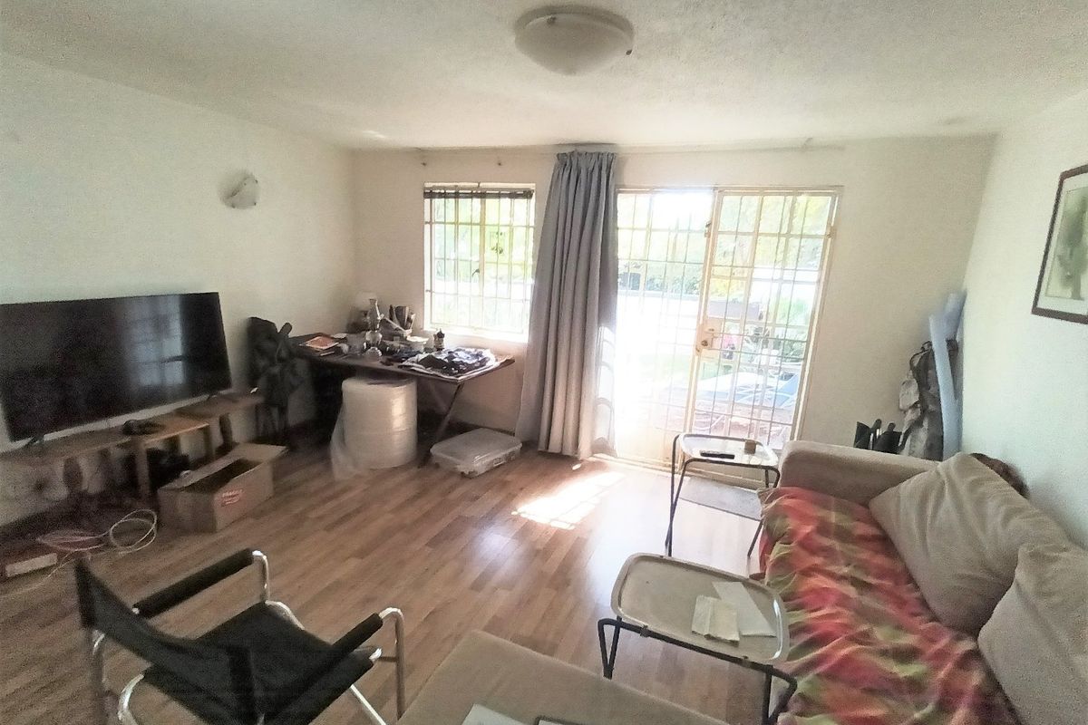A living room featuring laminate flooring, security bars on windows, and a sliding door leading to the exterior.