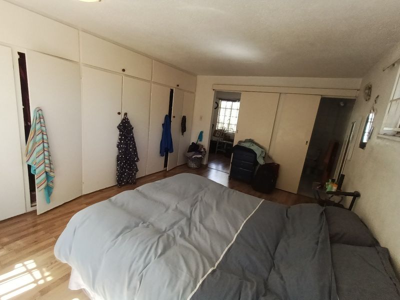 A bedroom featuring extensive built-in cupboard storage and laminate flooring, with an adjoining space visible through a sliding door.