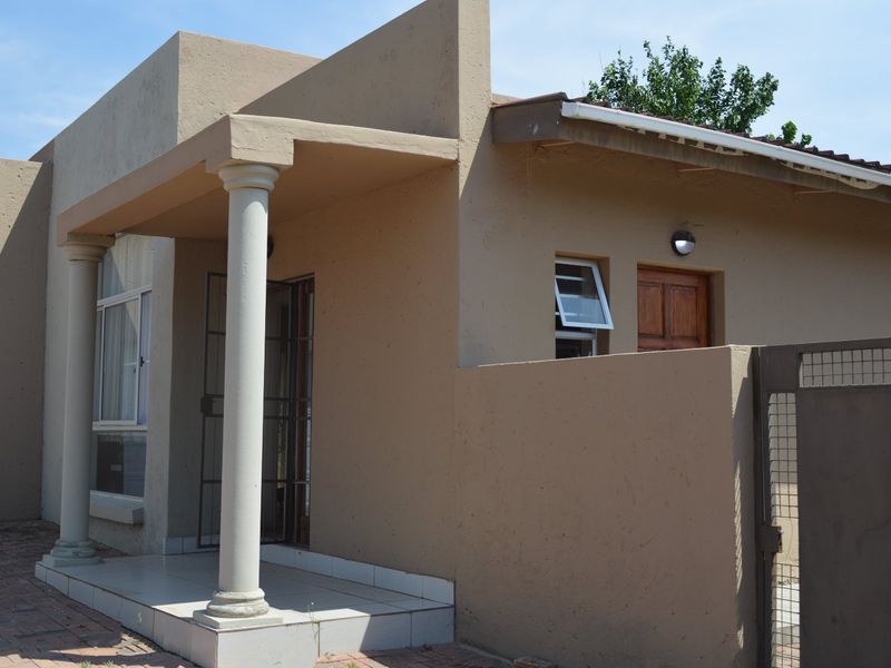 Front elevation of a townhouse featuring a covered entrance porch with classical columns, paved driveway, and secure access points.