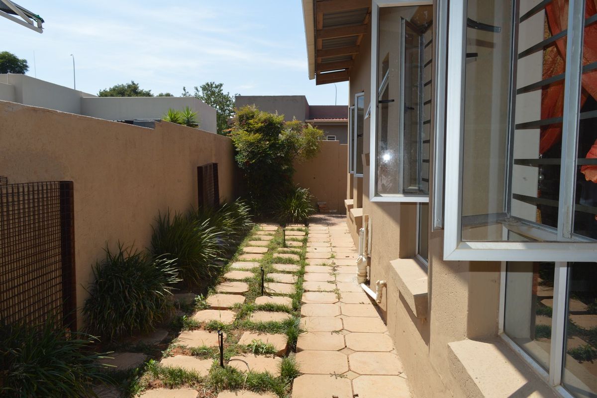 A side exterior walkway featuring paved paths, boundary walls, and casement windows with security bars.