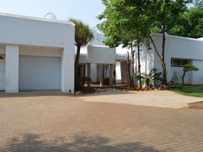 Front elevation of a modern house featuring a paved driveway, double garage, and a covered entrance area with established trees and garden.