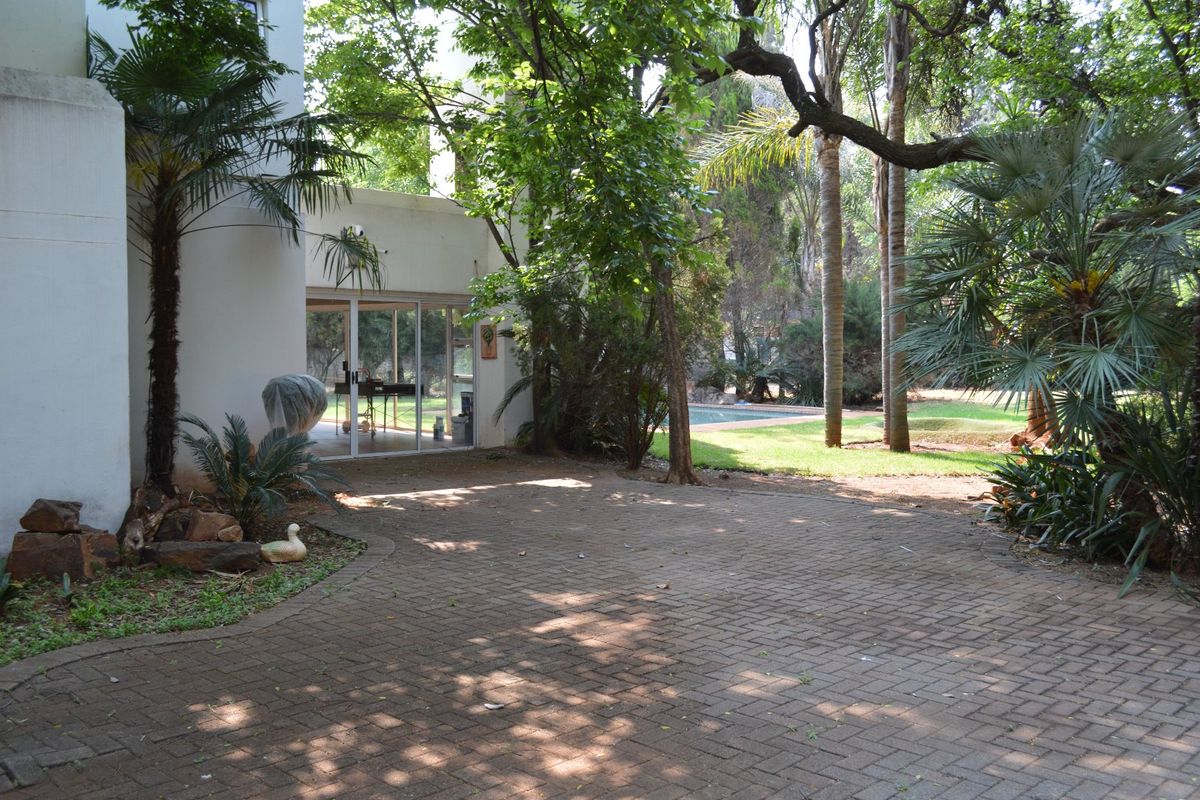 A spacious rear exterior area featuring a paved patio, sliding glass doors leading into the home, and a lush garden with a swimming pool.