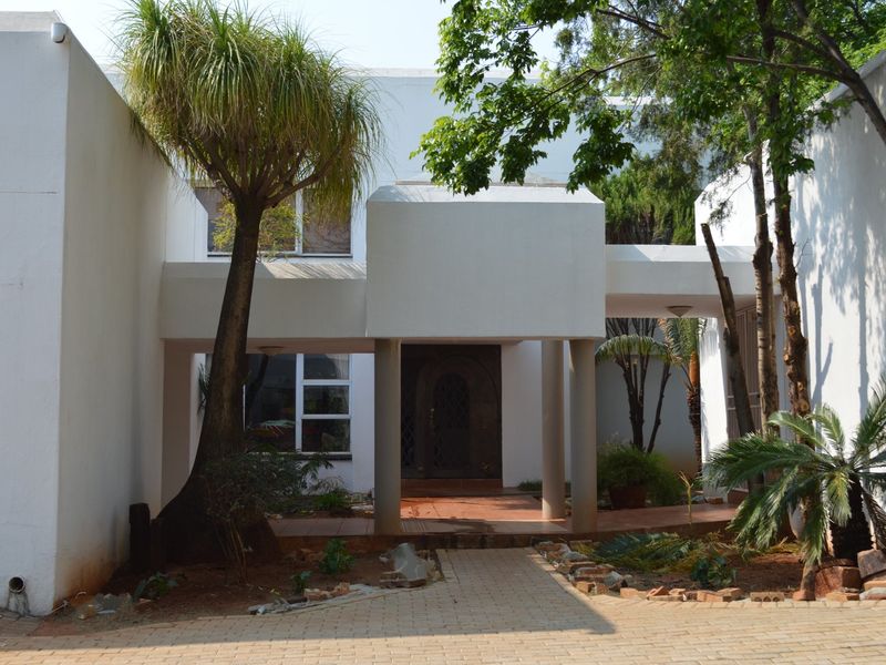 Front elevation of a modern-style house featuring a covered entrance, paved driveway, and established garden area.