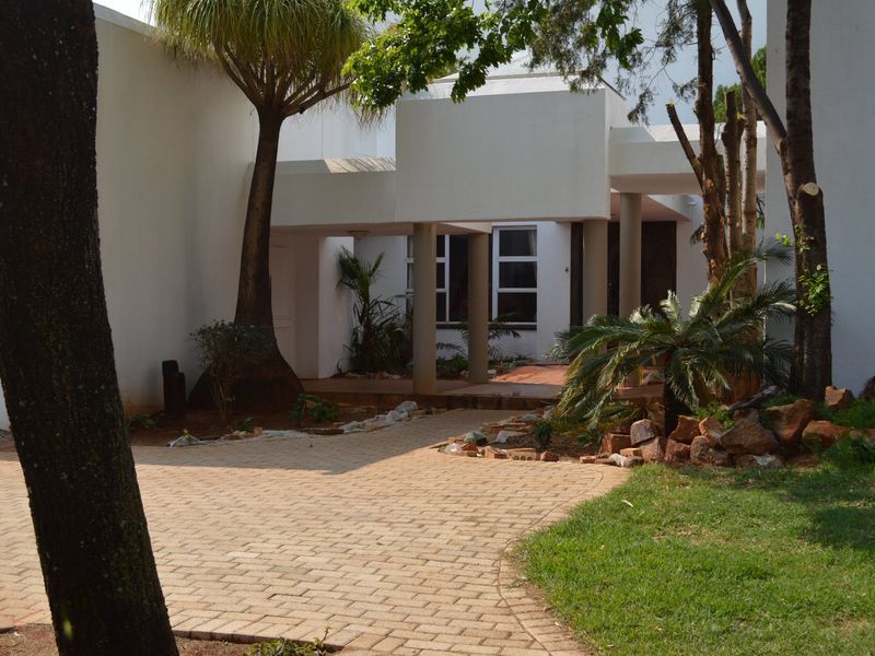 Front exterior view of the property featuring a paved driveway, covered entrance with structural columns, and established garden landscaping.