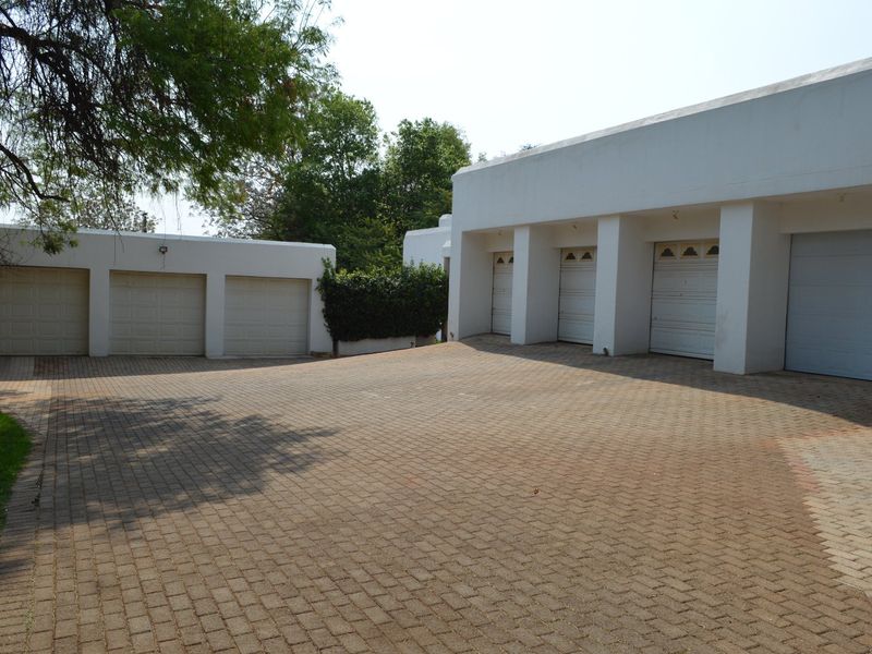 Spacious exterior view featuring a large paved driveway and multiple garage bays with white facade finishes.