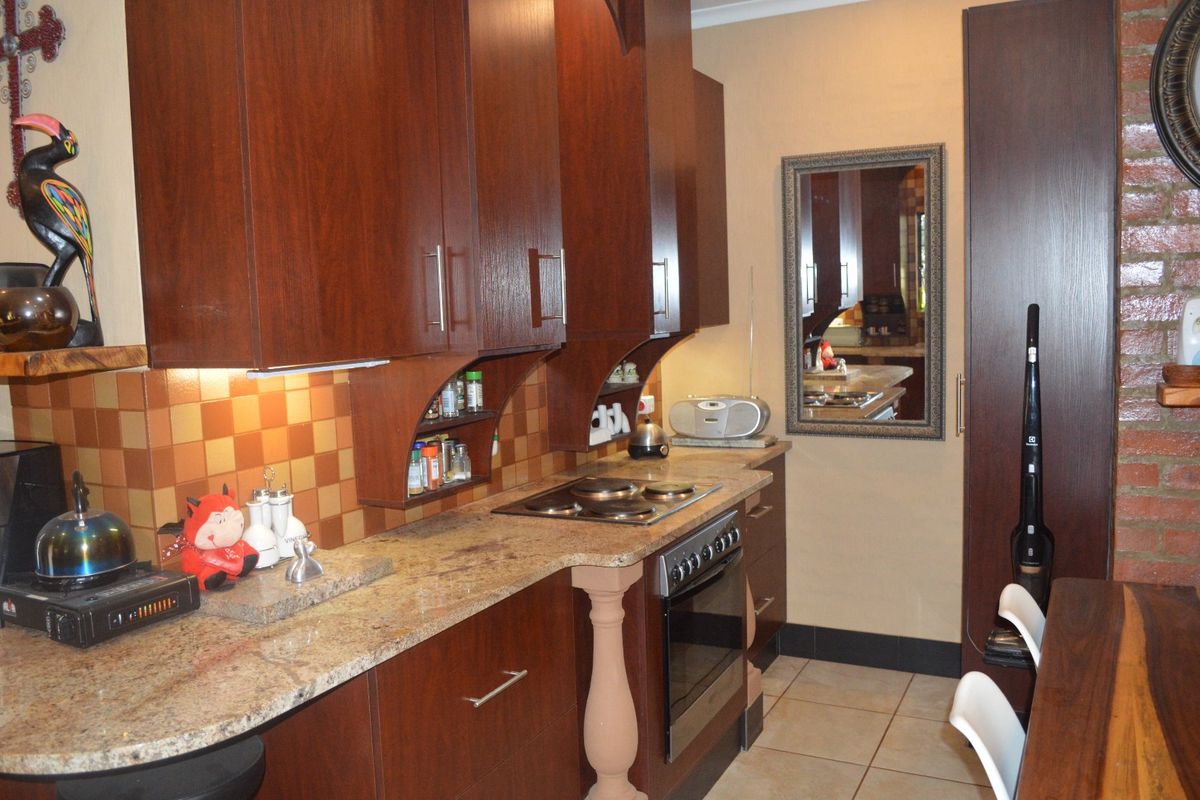A functional kitchen featuring dark wood cabinetry, granite countertops, a built-in oven and hob, and a decorative exposed brick wall.