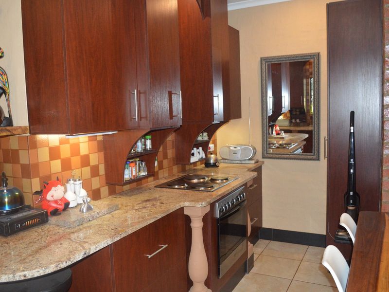 A functional kitchen featuring dark wood cabinetry, granite countertops, a built-in oven and hob, and a decorative exposed brick wall.