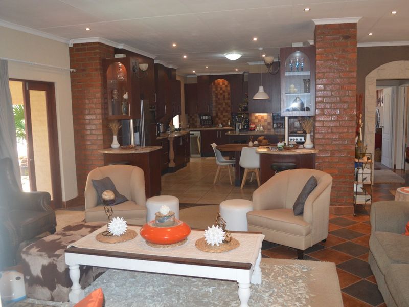 Spacious open-plan living and kitchen area featuring exposed brick columns, tiled flooring, and dark wood cabinetry with integrated kitchen storage.
