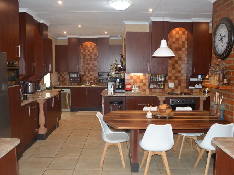 Spacious open-plan kitchen and dining area featuring dark wood cabinetry, granite countertops, tiled floors, and a distinctive exposed brick feature wall.