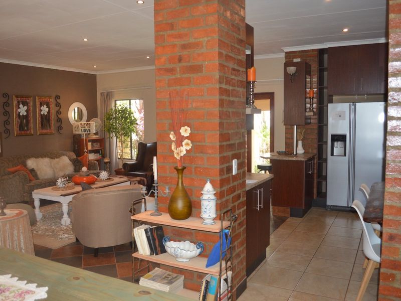 Open-plan living and kitchen area featuring a prominent exposed brick pillar, tiled flooring, and dark wood cabinetry.